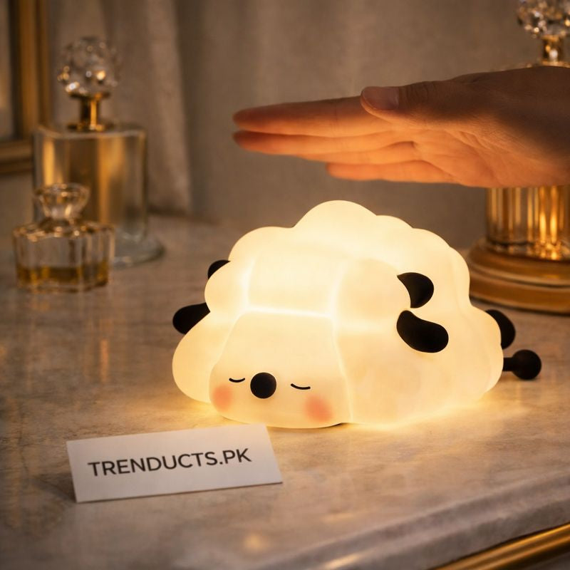 A glowing, squishy sheep-shaped silicone lamp with a calm sleeping face on a marble bedside table.