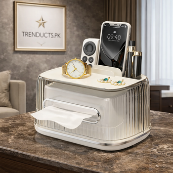 A modern white tissue box organizer featuring side compartments for remotes and a smartphone, sitting on a wooden desk.