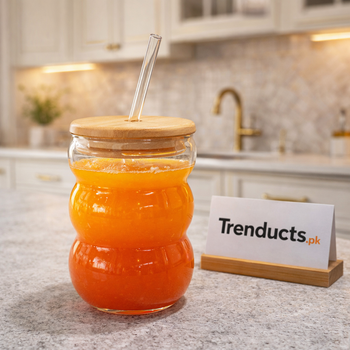 Aesthetic 500ml triple bubble shaped glass with bamboo lid and glass straw filled with orange juice on a kitchen counter - Trenducts Pakistan