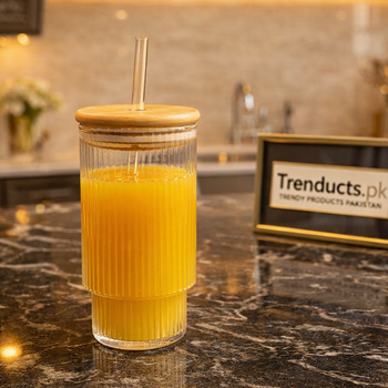 Aesthetic 500ml vertically ribbed iced tea glass with bamboo lid and glass straw filled with orange juice on a dark marble counter - Trenducts Pakistan