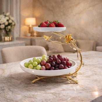 A 2-tier white ceramic cake stand with gold-edged borders and a gold center handle, displaying colorful macarons.