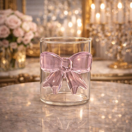 Transparent glass cup with a large 3D pink glass bow attached to the side, styled with a latte and dessert.