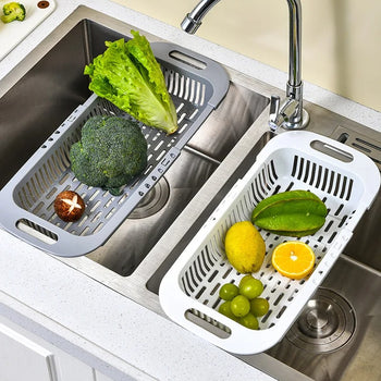 An expandable sink drain basket extended across a kitchen sink, filled with fresh vegetables.
